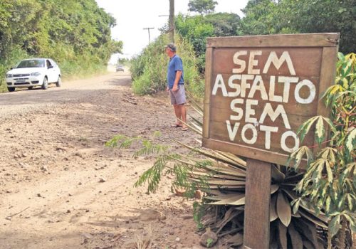 Valdemar Lisboa instalou placa em frente à residência e avisa: "Sem asfalto, ninguém ganha nosso voto." (Foto: Rodrigo Martini)